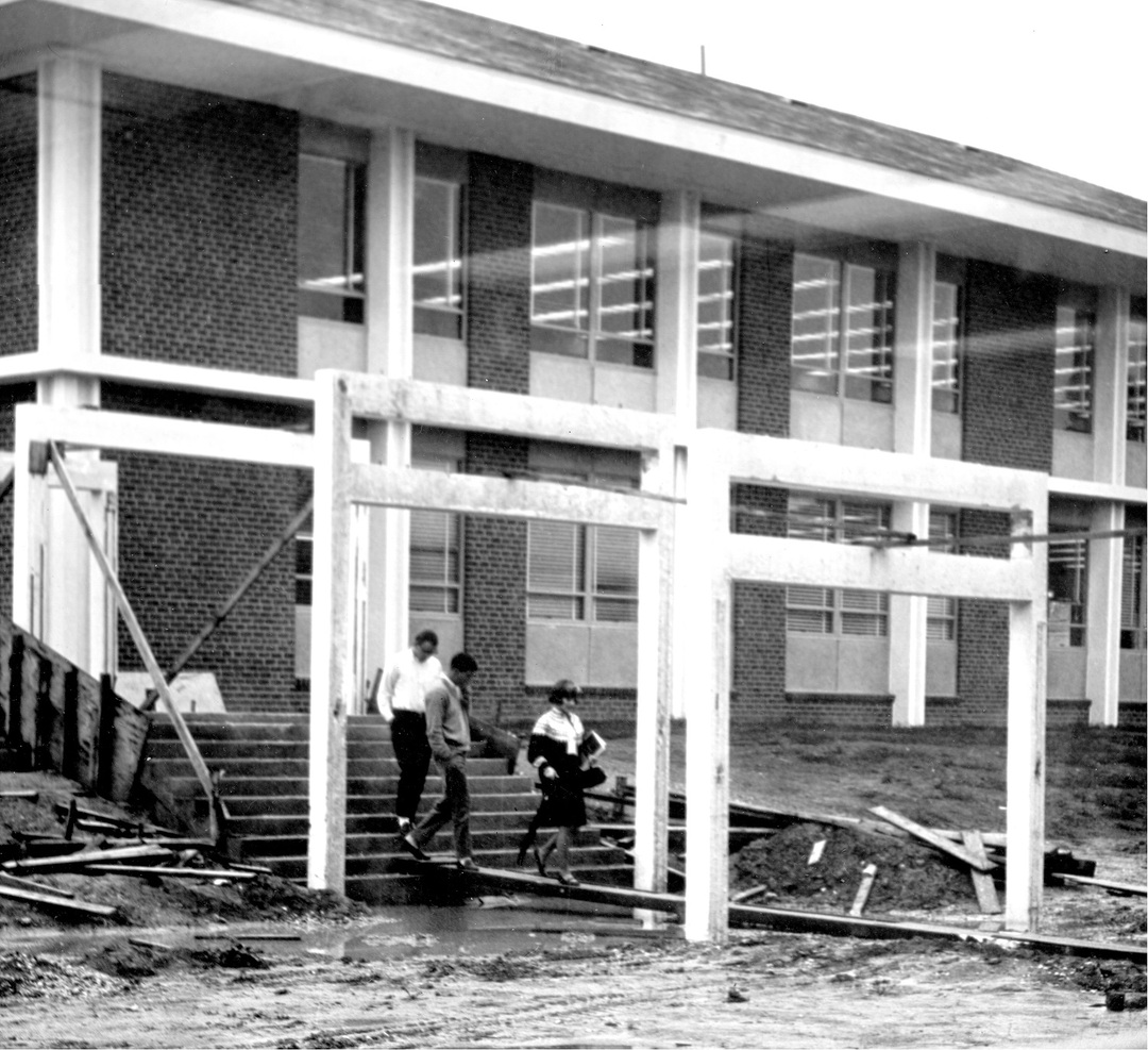 Students walk on wooden planks between buildings